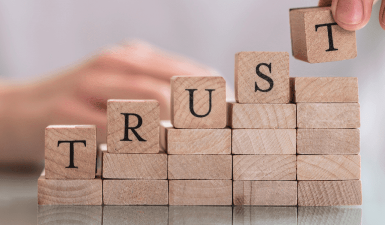 The word trust made up on wooden blocks which are stacked on a table to form a step.