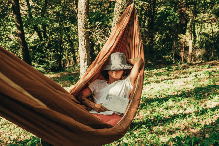 a woman sitting in a hammock reading a book.