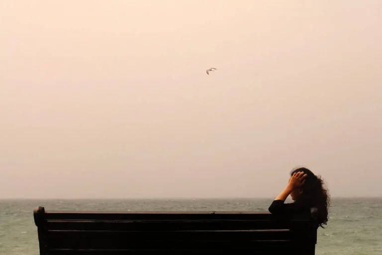 a woman sitting on a bench looking out at the ocean.