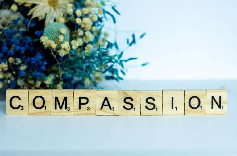 a wooden block with the word compassion next to a bouquet of flowers.