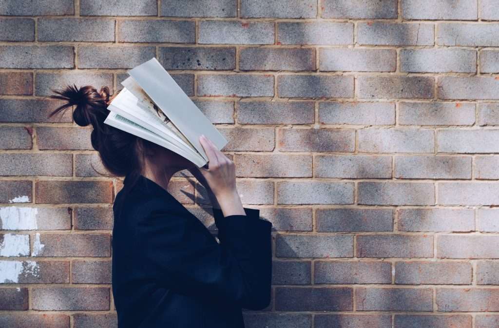 a woman holding a book against a brick wall.